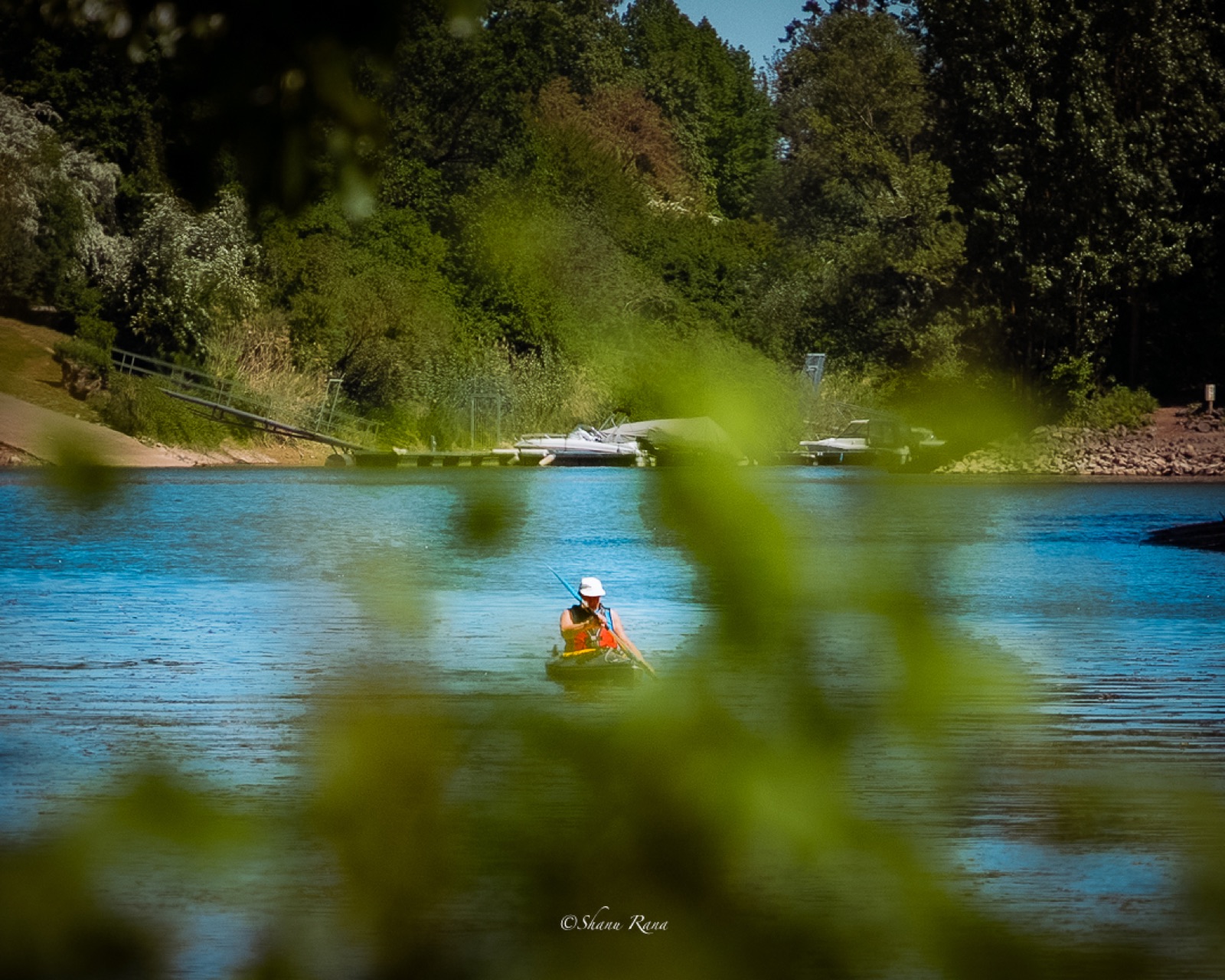 Kayaker on a blue river seen through green leaves
