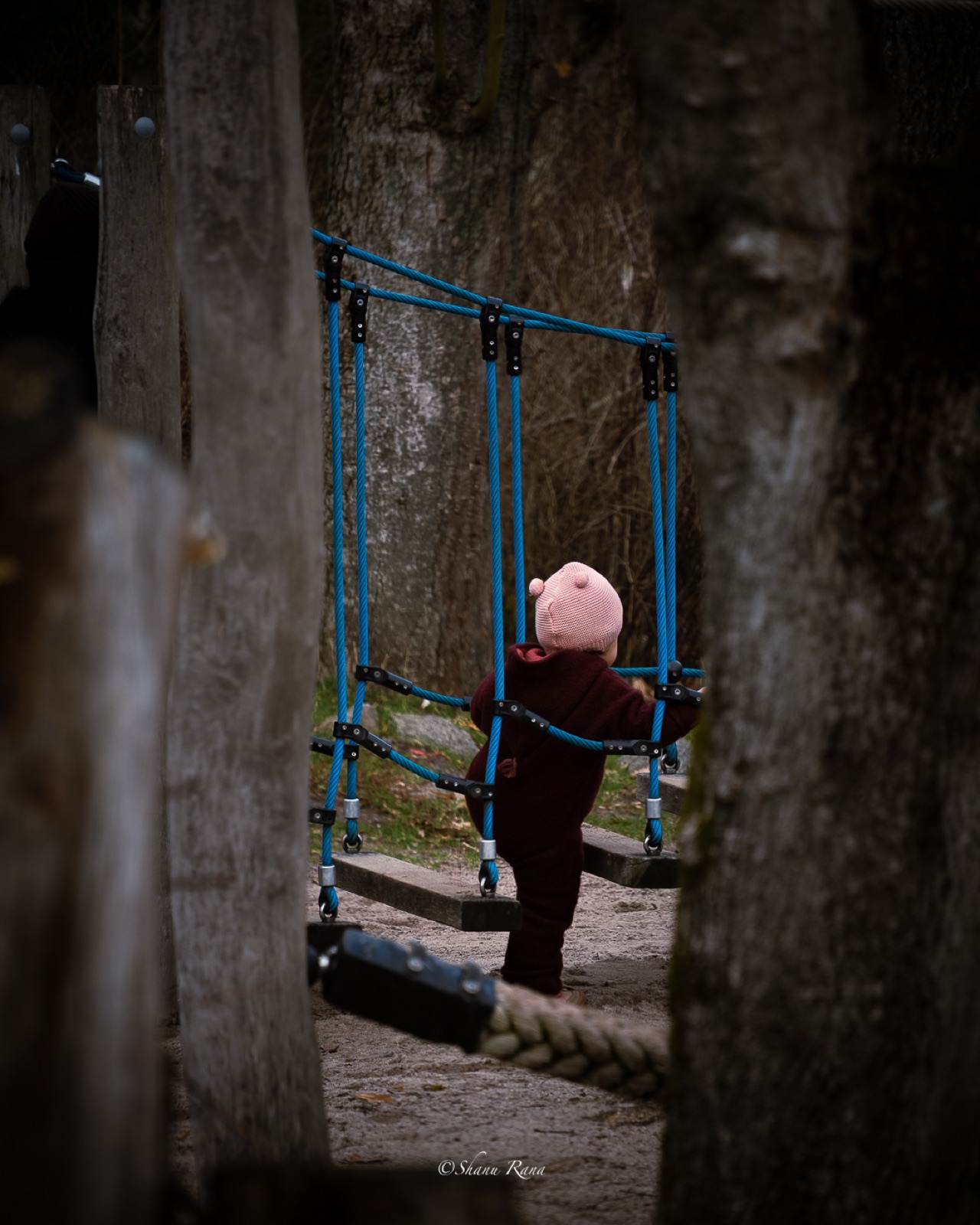 Toddler in a pink hat crossing a playground rope bridge