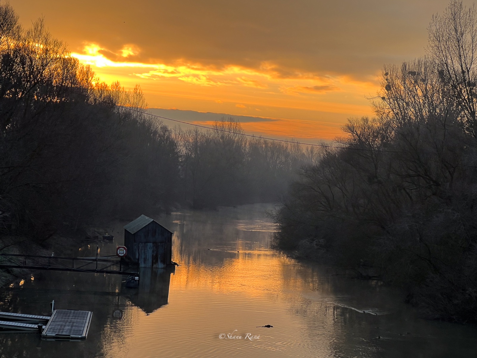 Golden sunrise over a calm river with boathouse