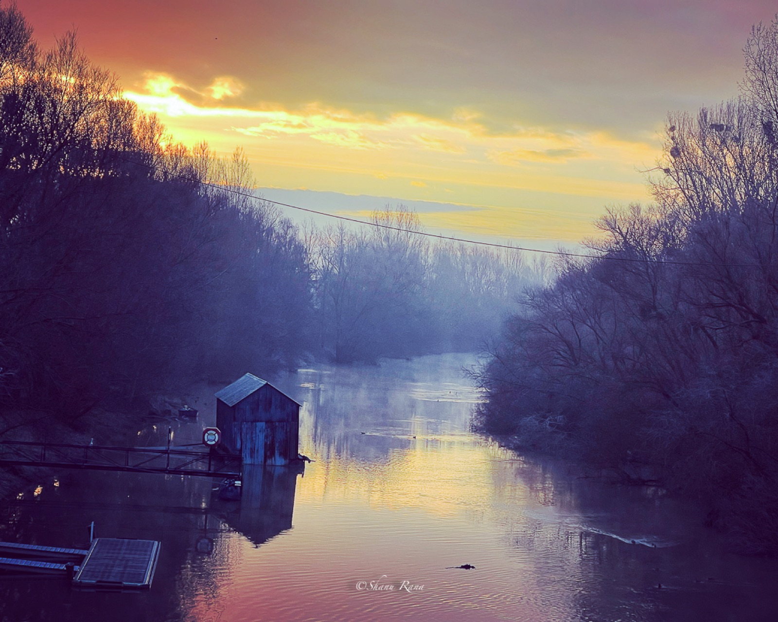 Misty river with old boathouse at dawn