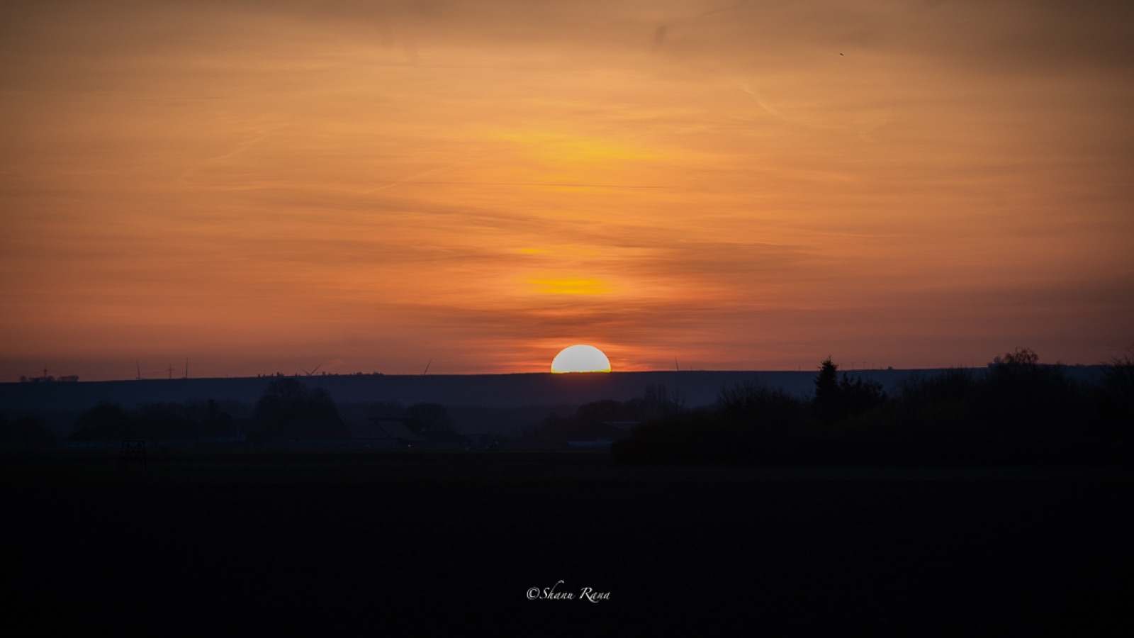Sun setting over dark fields with orange sky