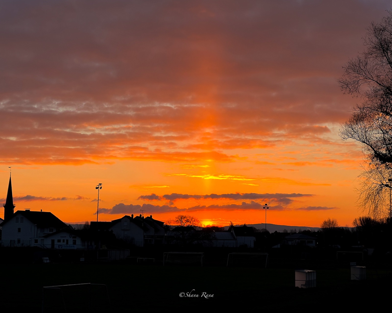 Fiery sunset with a light pillar over village rooftops